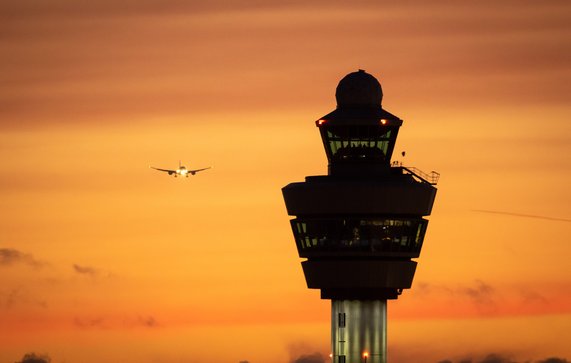 Airport control tower with a airplane landing in the background during sunset. door VanderWolf Images (bron: shutterstock)