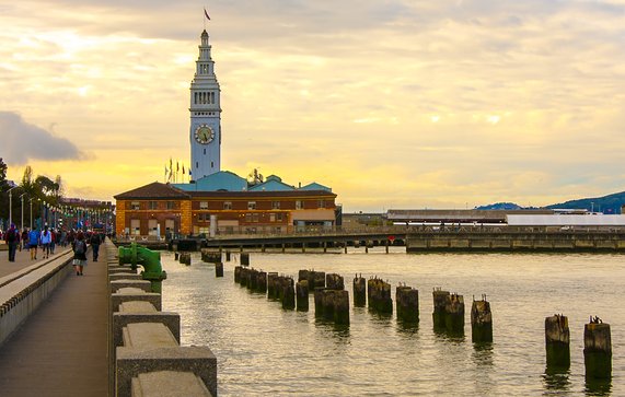 Postcard-like image of the boardwalk/embarcadero leading to the Ferry Building in San Francisco. The sky is highlighted with gorgeous yellow pre-sunset cloud covering. door dlove (bron: shutterstock)